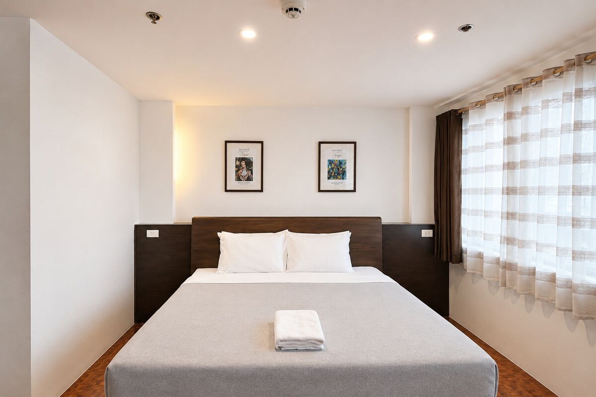 Habitación de hotel con una cama, dos cuadros en la pared y una ventana con cortinas.