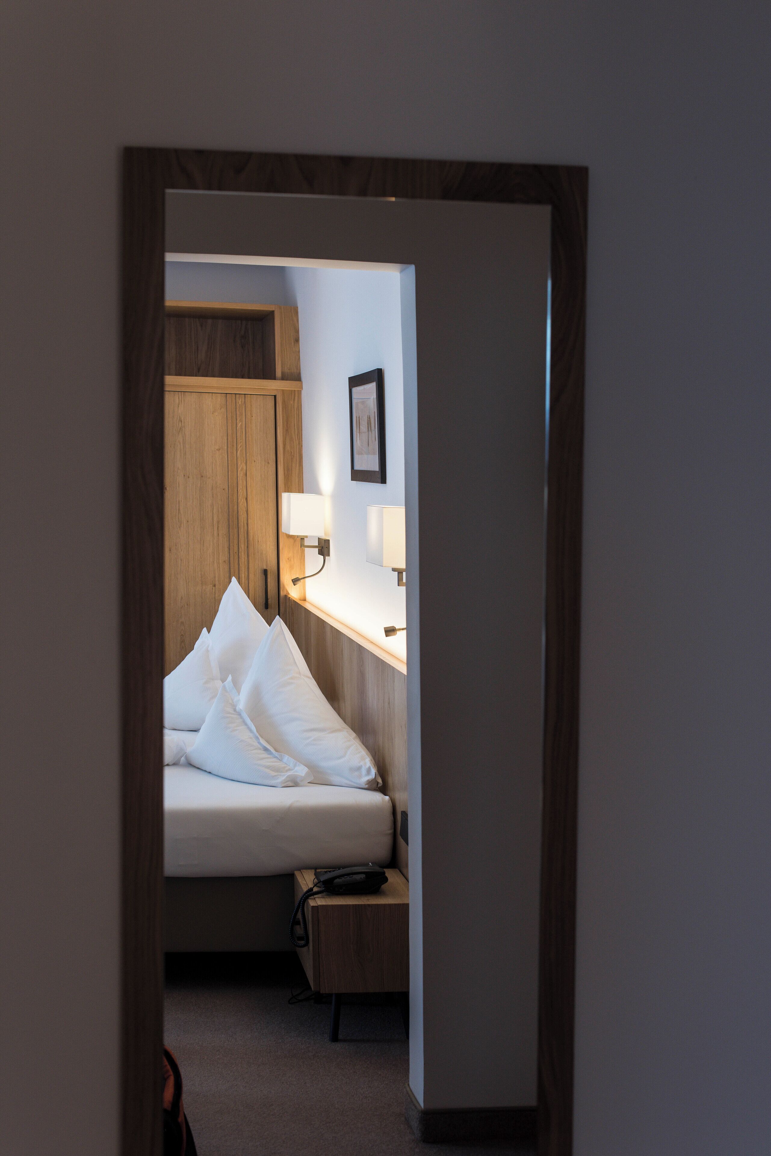 Una habitación de hotel con cama, mesita de noche, lámpara y un armario de madera.