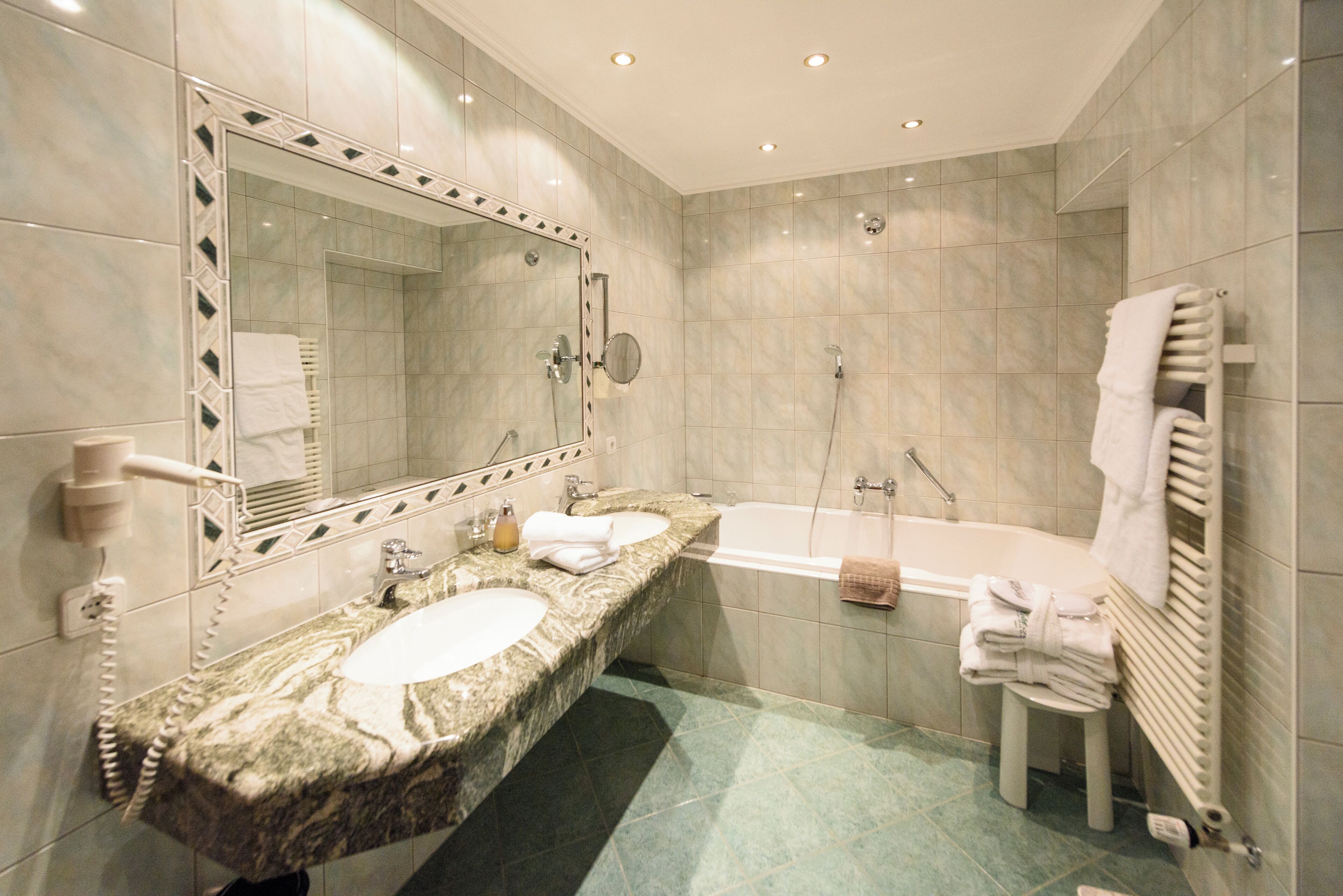 A bathroom with two sinks, a large mirror, a bathtub, and a towel rack.