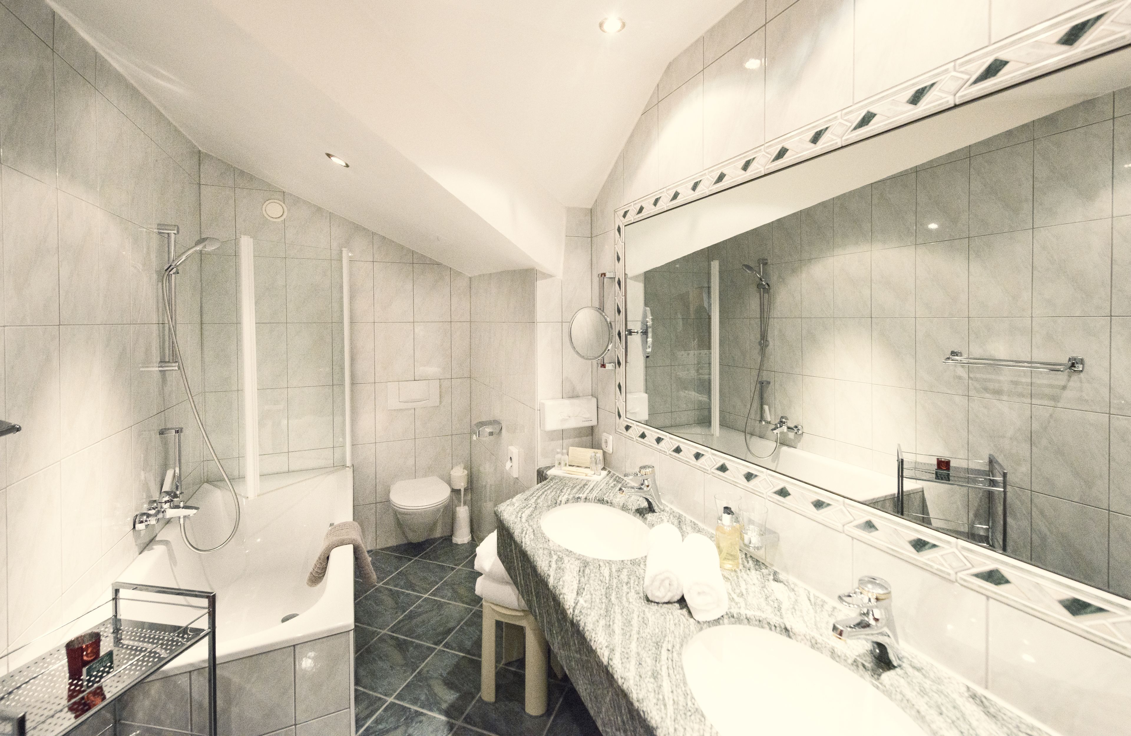 A modern bathroom with a large mirror, two sinks, a shower, and a toilet.