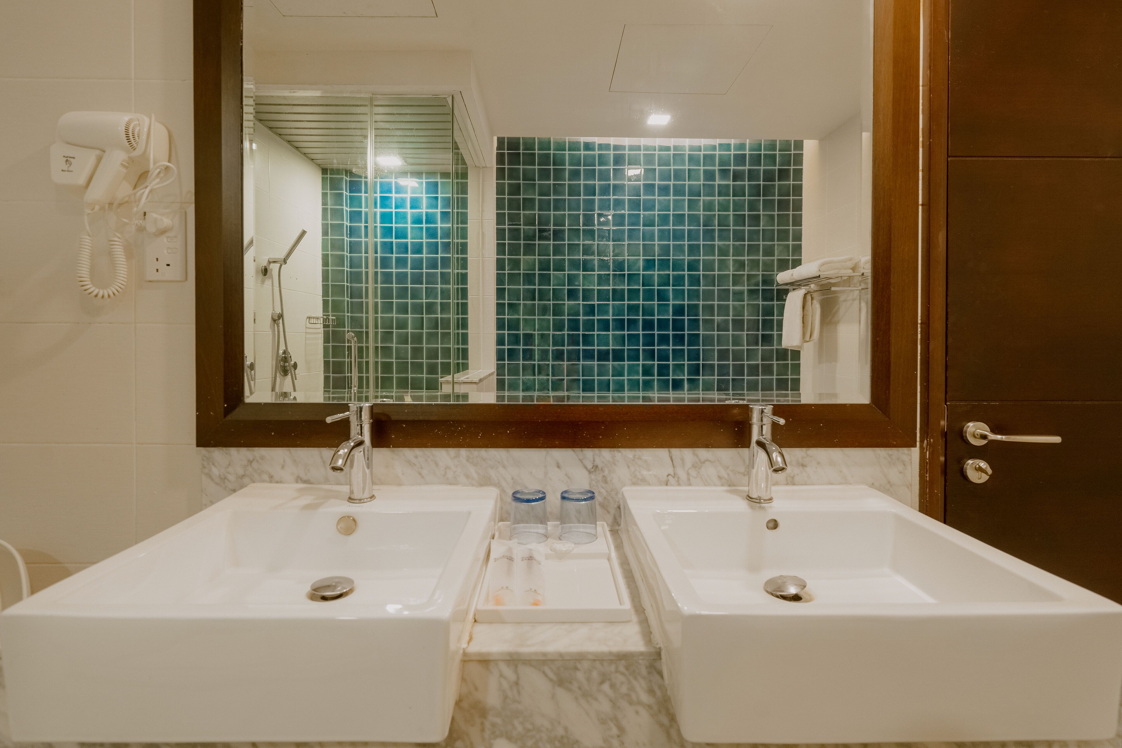 Un baño con dos lavamanos, un secador de pelo, un espejo y una zona de ducha.