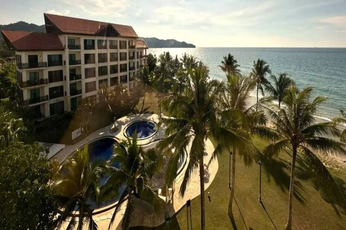 A resort with a pool area, palm trees, and a view of the sea.