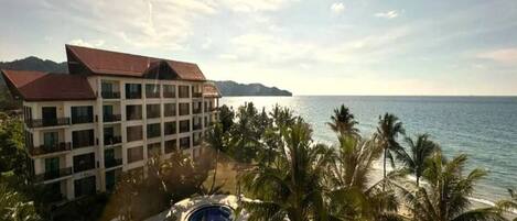 A resort with a pool area, palm trees, and a view of the sea.