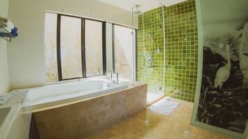 Een moderne badkamer met een groot bad, een douchecabine met glazen wanden en een groene betegelde muur.