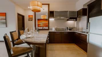 A modern kitchen with dark cabinetry, a marble countertop, and a built-in oven. There are two pendant lights hanging above the island, and a painting of a sunset on the wall.