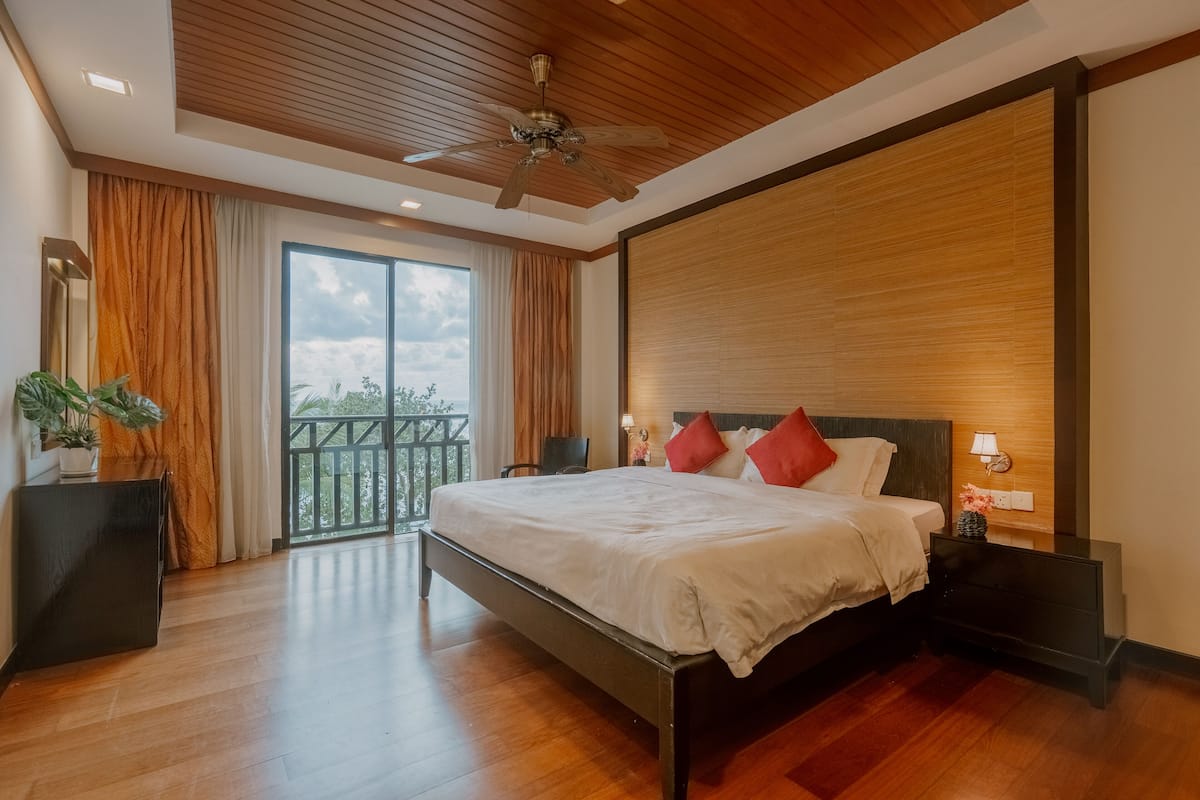 A modern bedroom with a large bed, wooden ceiling, and a balcony view.
