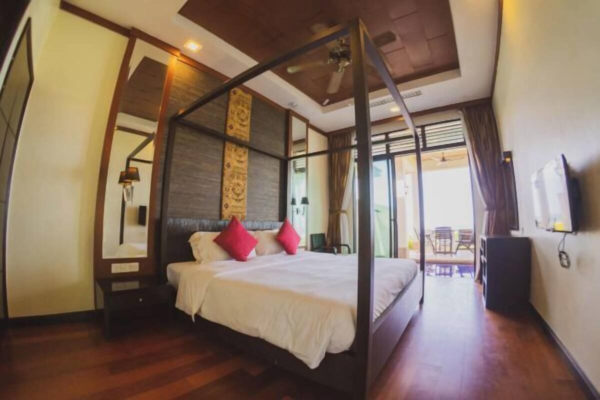A room with a four-poster bed, a wooden floor, a ceiling fan, and a view of the outside.