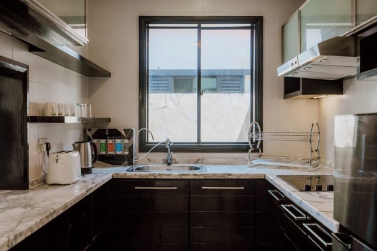 Una cocina moderna con un ventanal grande, armarios oscuros y un refrigerador de acero inoxidable.
