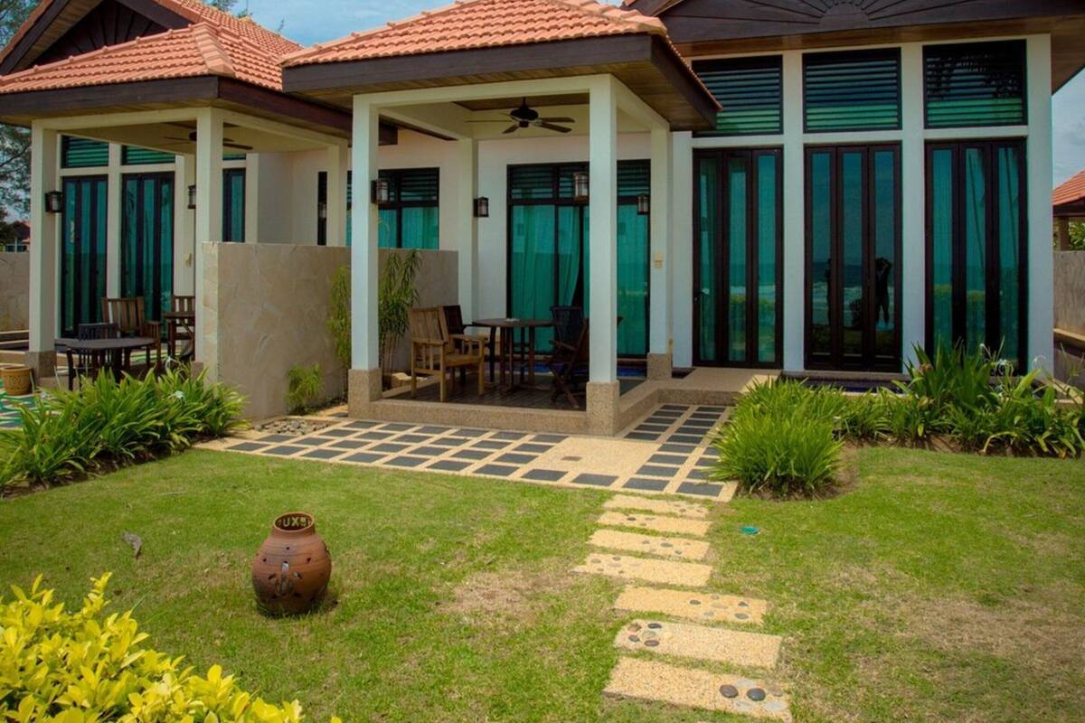 A modern two-story house with a tiled roof, large windows, and a covered patio area with outdoor furniture.