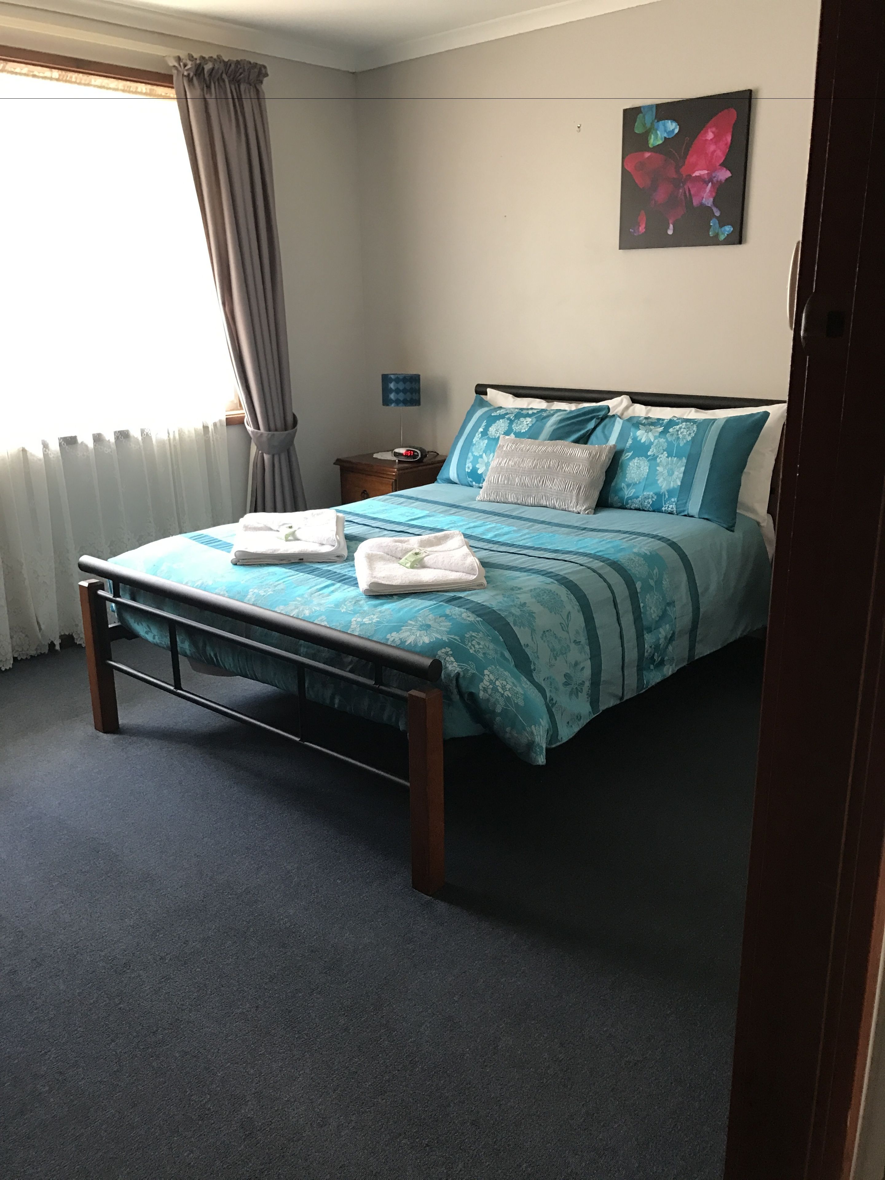 Quarto bem arrumado com cama, mesa de cabeceira, luminária e um quadro na parede.