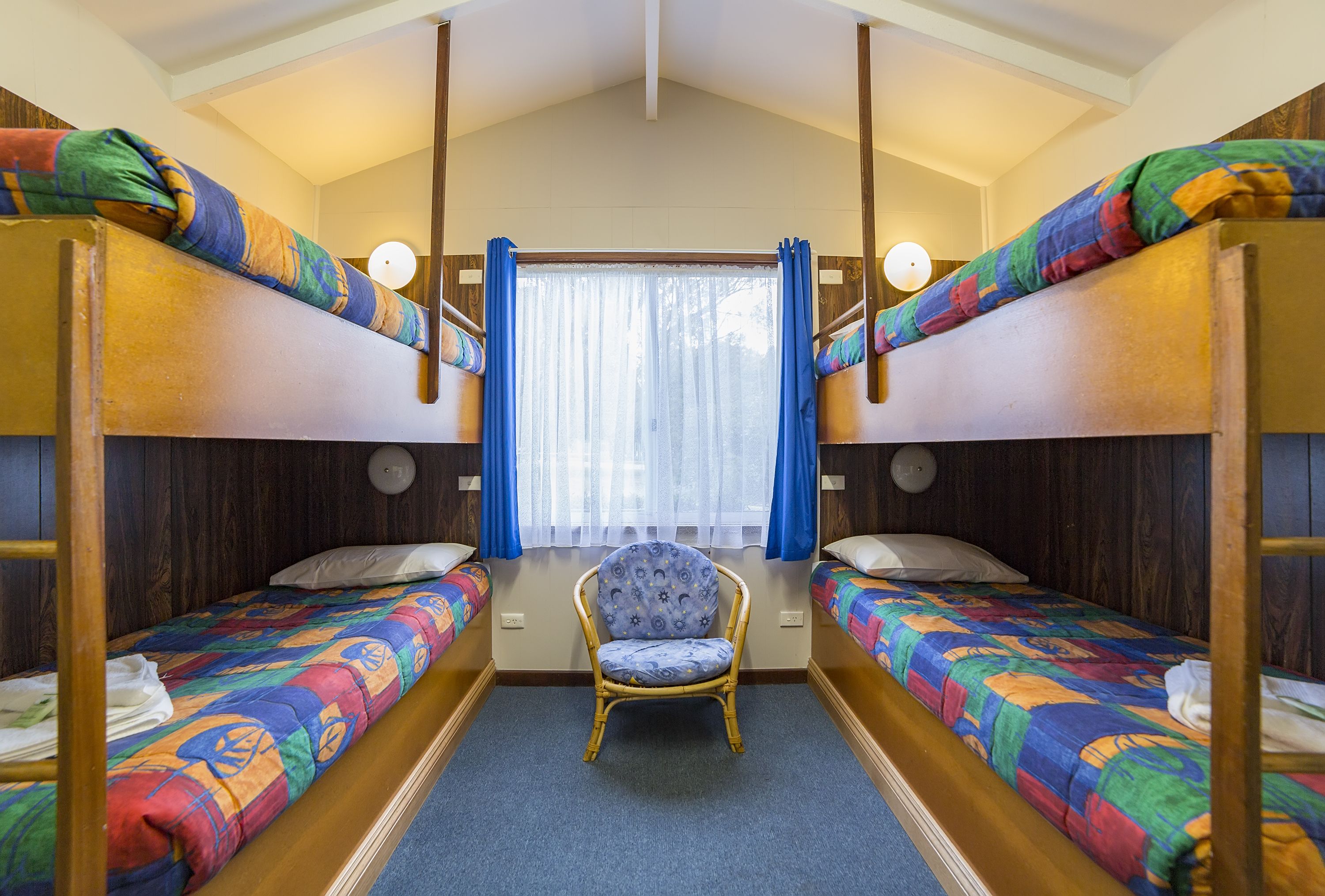 A bunk room with two beds, a chair, and a window with curtains.