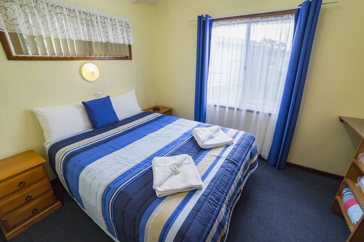 A neatly made bed with a blue and white striped bedspread and two folded white towels.