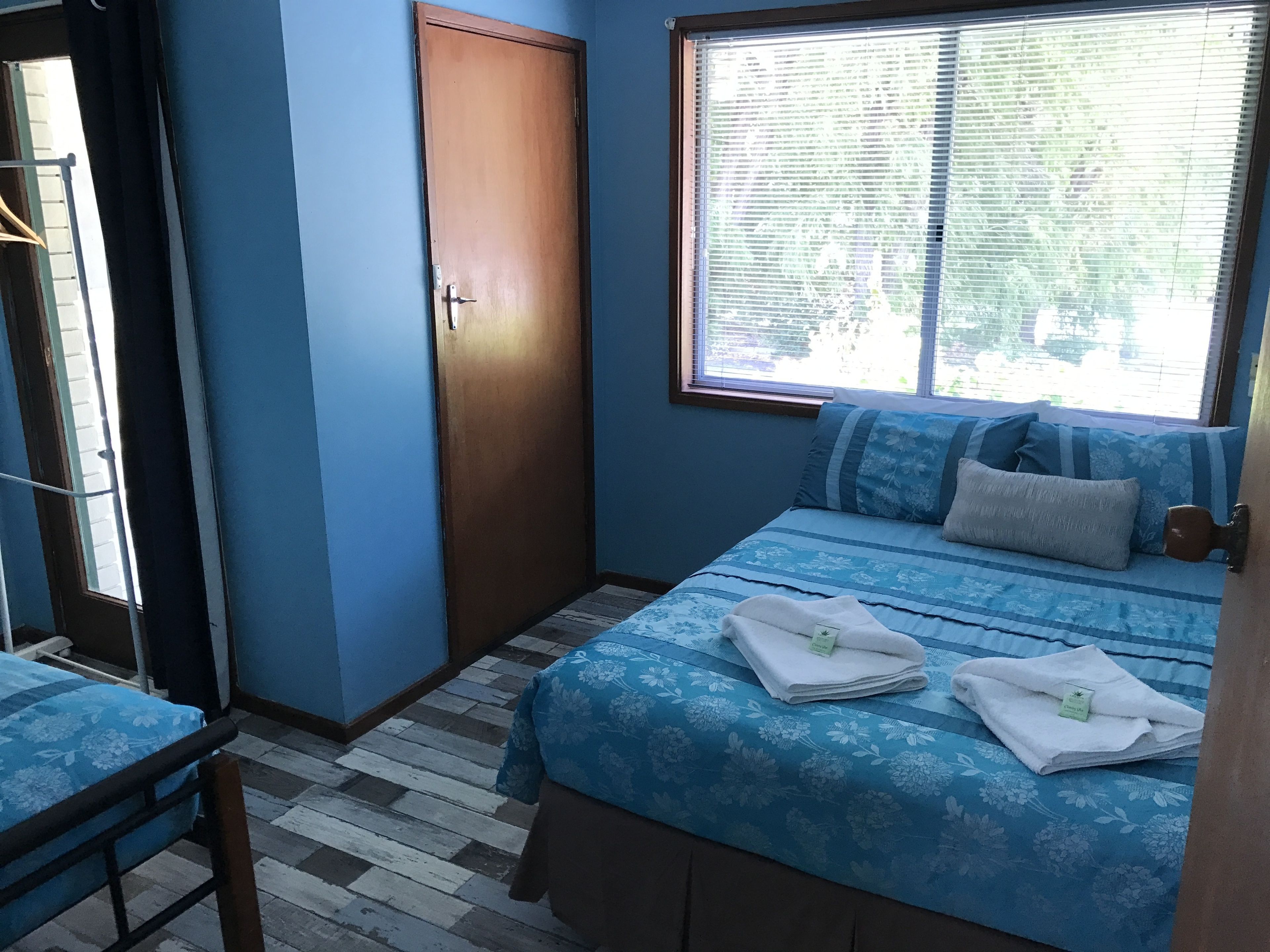 A bedroom with a bed, a window with blinds, a door, and a chair.