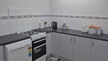 Een keuken met een gasfornuis, oven, witte kastjes, een zwart aanrecht en een vloer met een patroon.