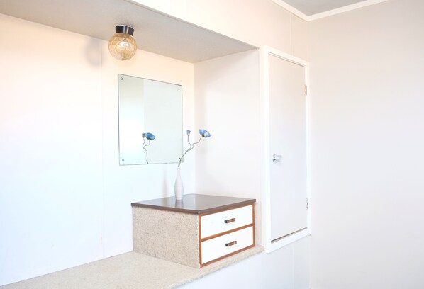 A room with a white wall, a wooden vanity with two drawers, a mirror, and a door. - Gateway International Motel (Rotorua)