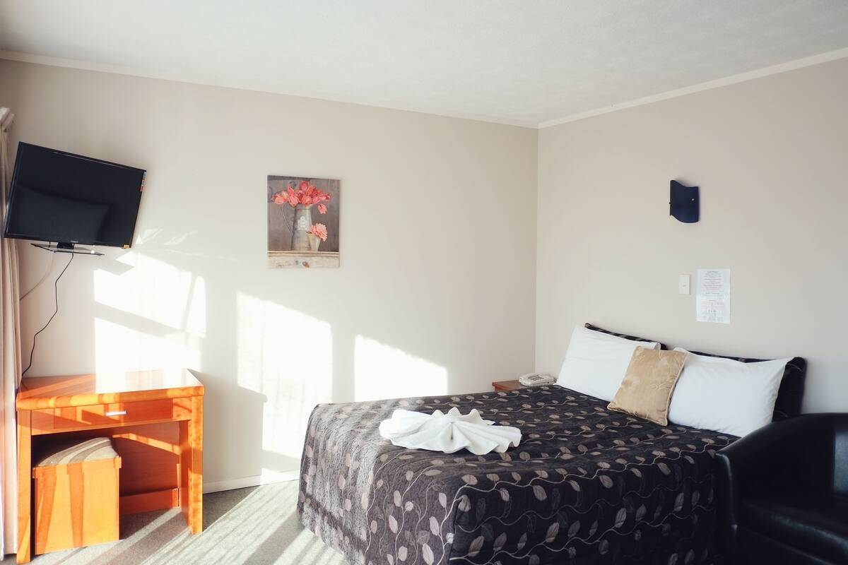 A hotel room with a bed, a desk, a television, and a painting on the wall.