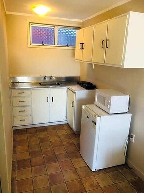 A compact kitchen with white cabinets, a sink, a microwave, and a dishwasher. - Gateway International Motel (Rotorua)