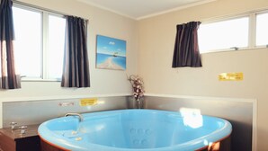 A room with a blue bathtub, a window with curtains, a beach painting, and a sign indicating a no-smoking policy. - Gateway International Motel (Rotorua)
