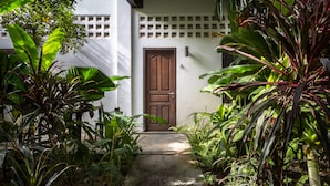 Un camí de formigó estret que condueix a una porta de fusta, envoltat de vegetació tropical exuberant.