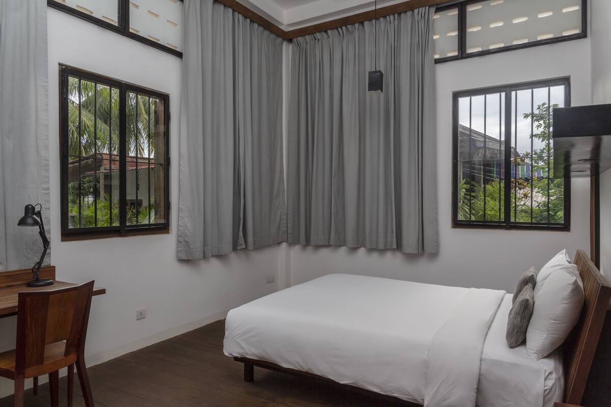 Ein Schlafzimmer mit einem Bett, einem Schreibtisch und zwei Fenstern.