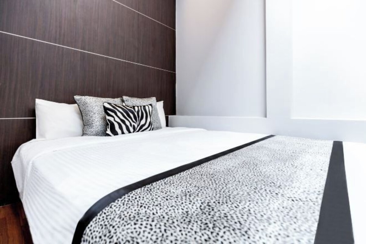 A modern bedroom with a large bed, dark wood headboard, and a white wall.