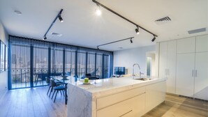Une cuisine moderne dotée d’un grand îlot central, d’un coin repas avec des chaises et de grandes fenêtres offrant une vue sur la ville.