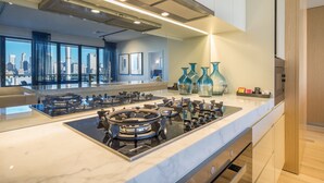 Une cuisine moderne dotée d’un îlot central, d’appareils électroménagers en acier inoxydable et offrant une vue sur la ville grâce à de grandes fenêtres.