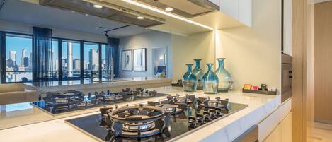 A modern kitchen with a central island, stainless steel appliances, and a city view through large windows.