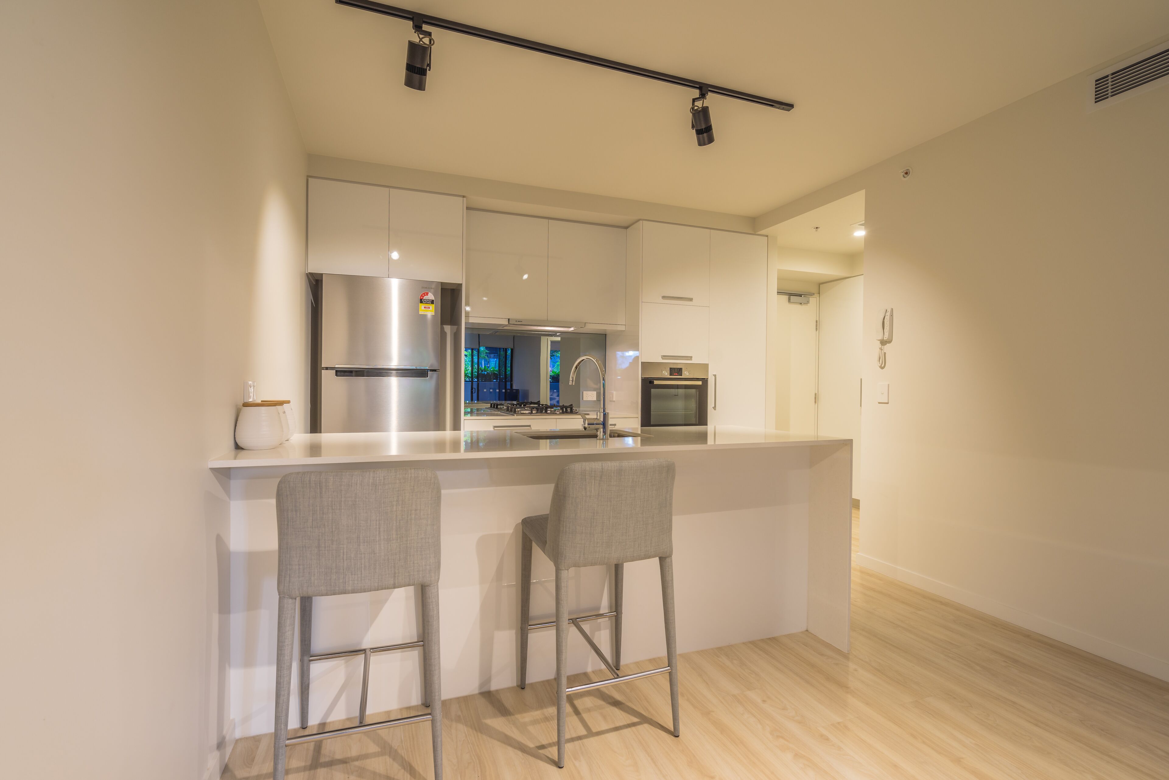 Une cuisine moderne avec des meubles blancs, des appareils en acier inoxydable et un coin bar équipé de deux tabourets.