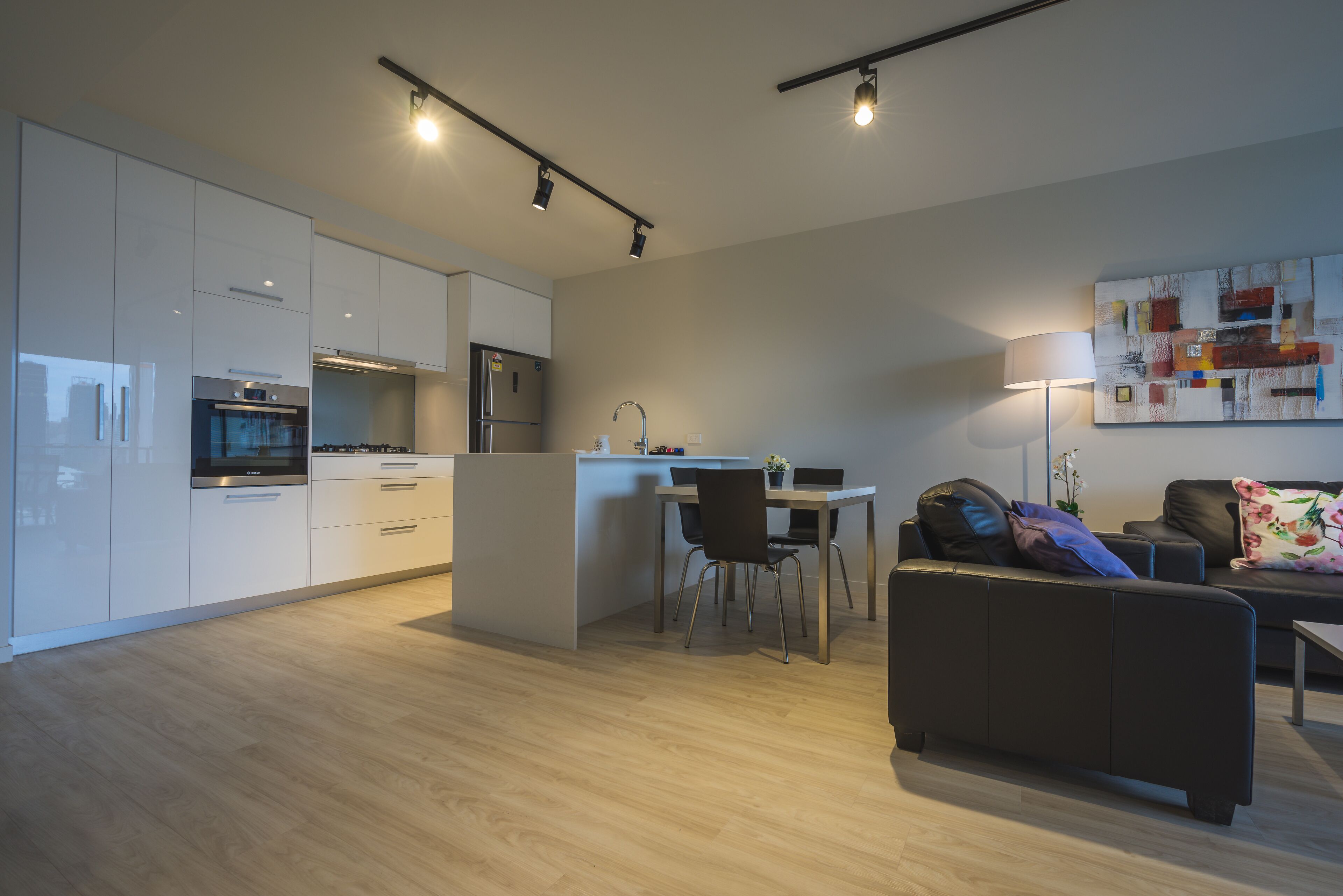 Eine moderne Küche mit weißen Schränken, ein Essbereich mit Tisch und Stühlen sowie ein Wohnbereich mit Sofa und Lampe.
