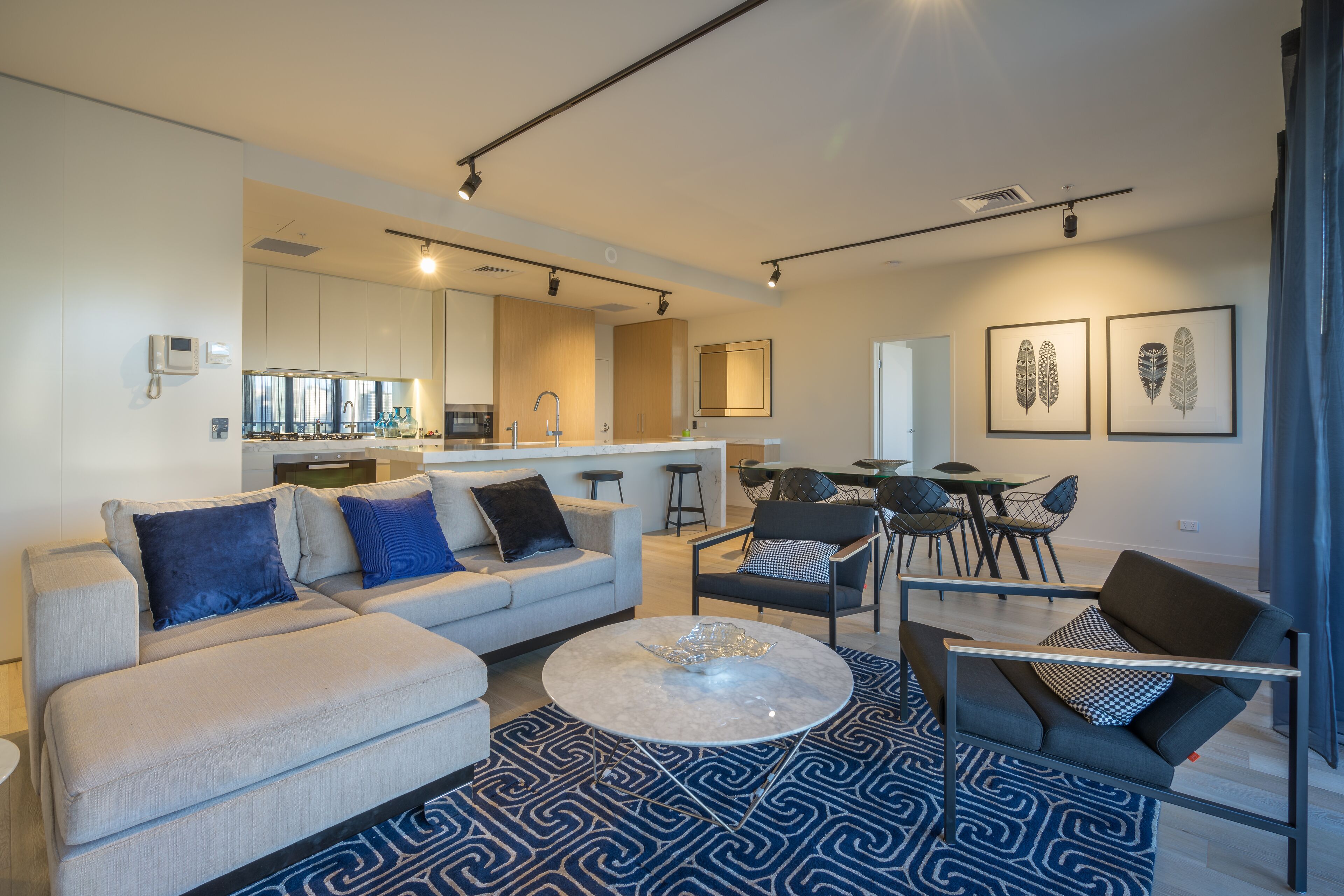 Een moderne woonkamer met een bank, salontafel en stoelen, een keuken met kasten en een eettafel, en kunstwerken aan de muren.