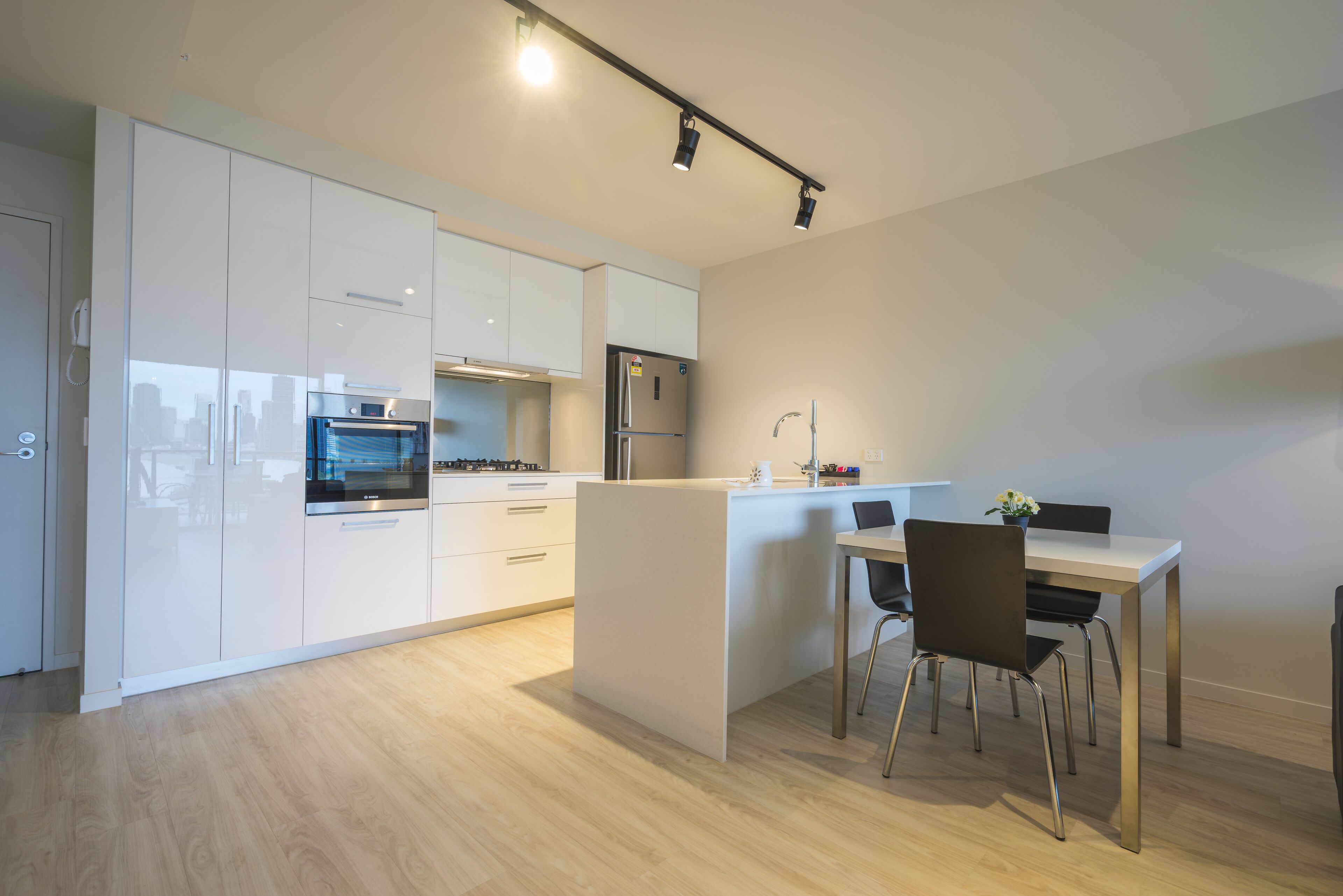 A modern kitchen with white cabinets, a built-in oven, and a dining area with a table and chairs.