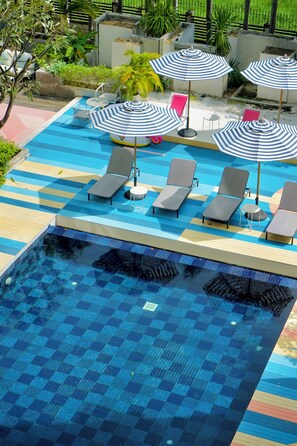 Relax by the pool surrounded by lush greenery and shaded lounge chairs.
