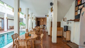 A spacious indoor area with a pool, wooden tables and chairs, and a kitchen area. - Sedasa Lodge (Tibubeneng)