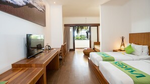A hotel room with a wooden desk, a television, two beds with green bedspreads, a large painting of a beach, and a view of the outdoors through a glass door. - Sedasa Lodge (Tibubeneng)