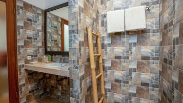 Un baño con pared de baldosas de piedra, una escalera de madera, un lavamanos y dos toallas colgadas en la pared.