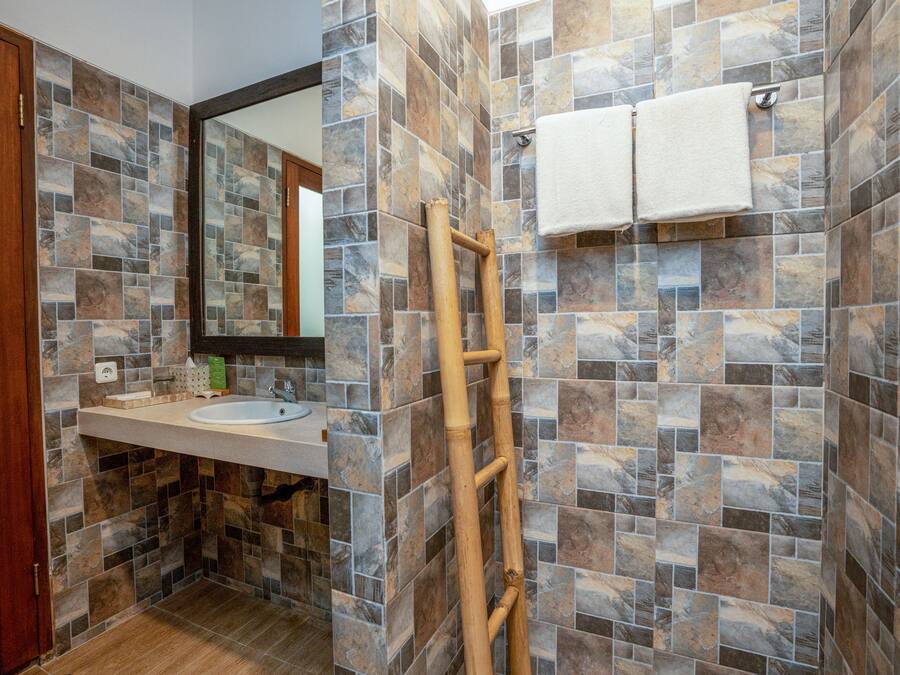 Un baño con pared de baldosas de piedra, una escalera de madera, un lavamanos y dos toallas colgadas en la pared.