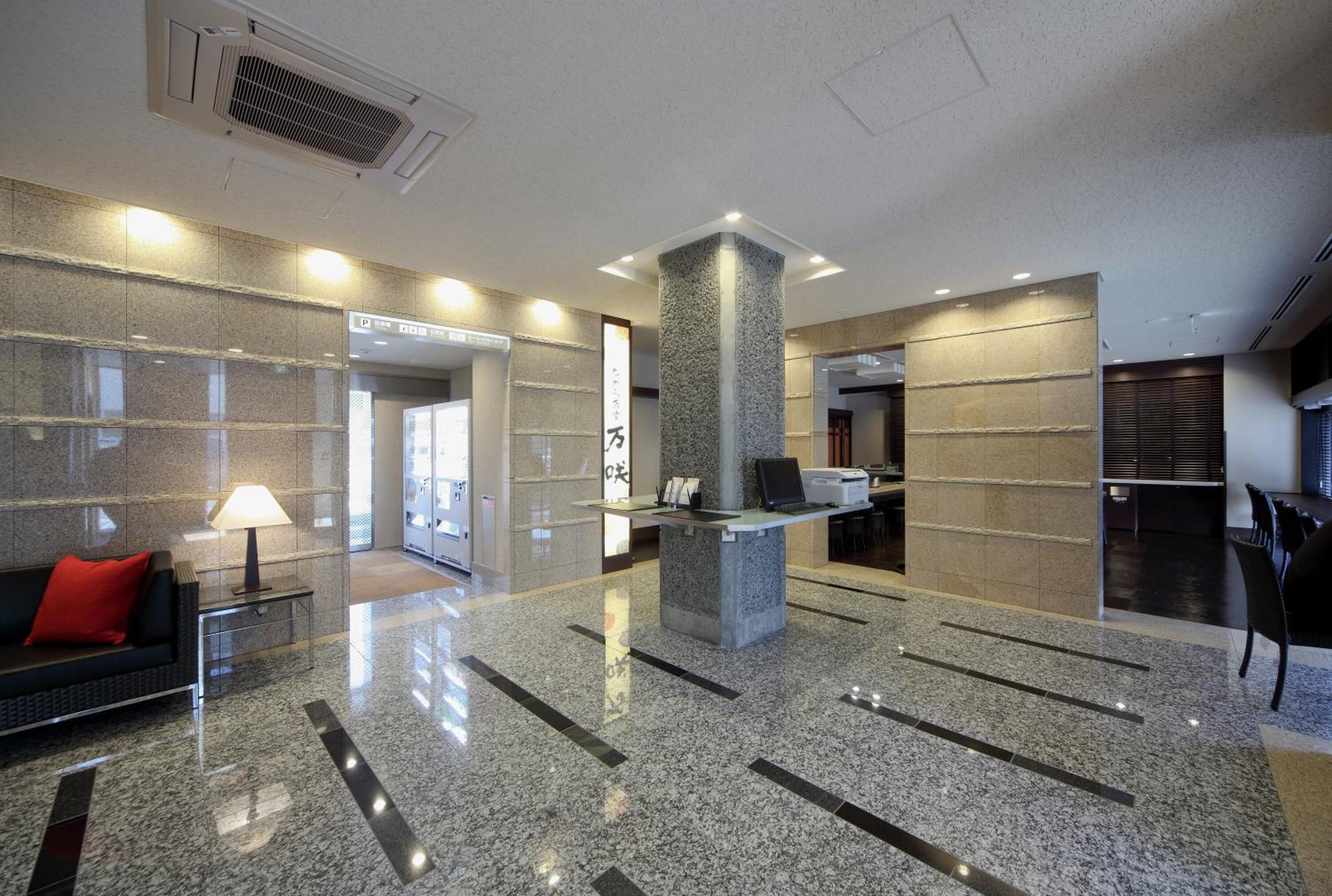A modern lobby with a reception desk, a red sofa, and a stone pillar.