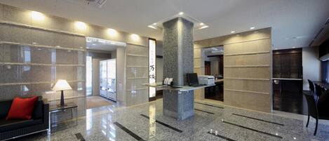 A modern lobby with a reception desk, a red sofa, and a stone pillar.