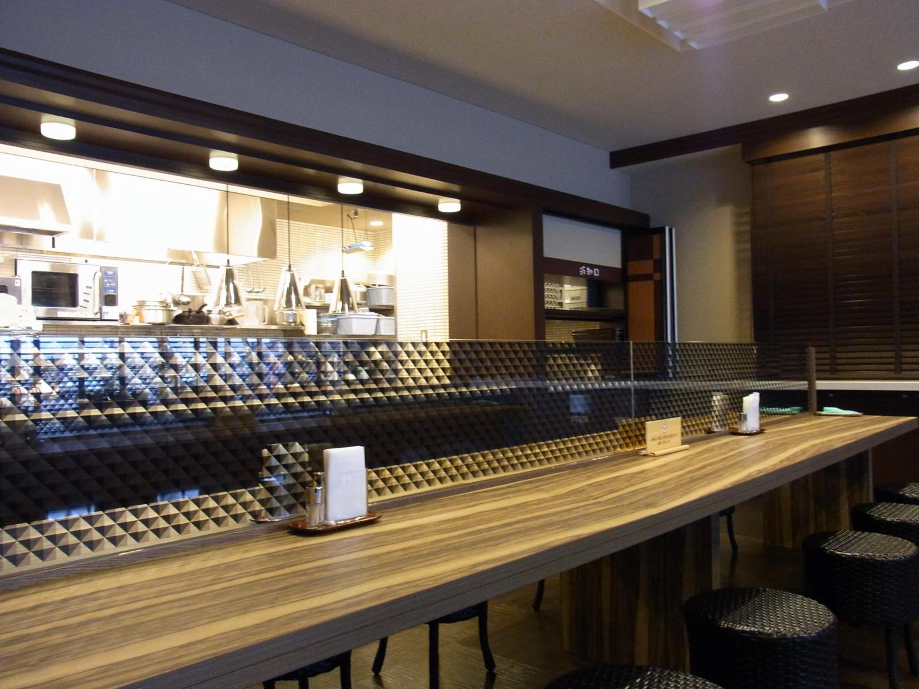 Uma área de bar moderna com um balcão comprido, banquetas estofadas pretas e uma cozinha ao fundo.