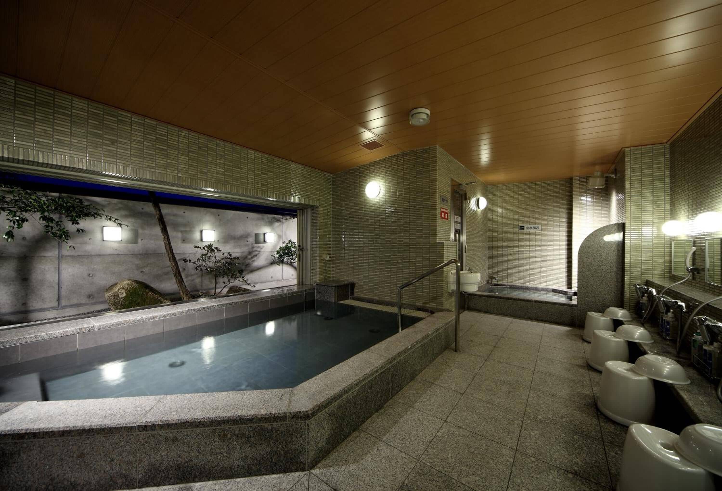 A modern spa with a large hot tub, tiled walls, and a wooden ceiling.