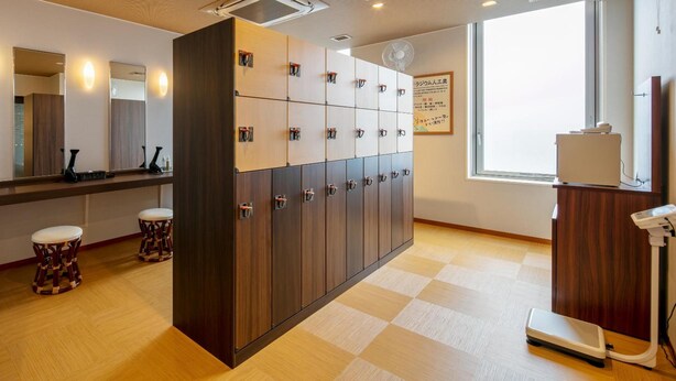 Hotelkamer met een grote spiegel, een houten kast met verschillende vakken, een weegschaal en een raam met uitzicht.