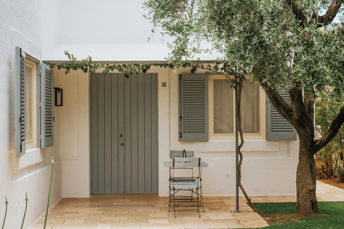 A building with a closed grey door, a small table, and a tree in the foreground.
