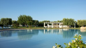 Una piscina con sillones de descanso y un edificio con terraza.