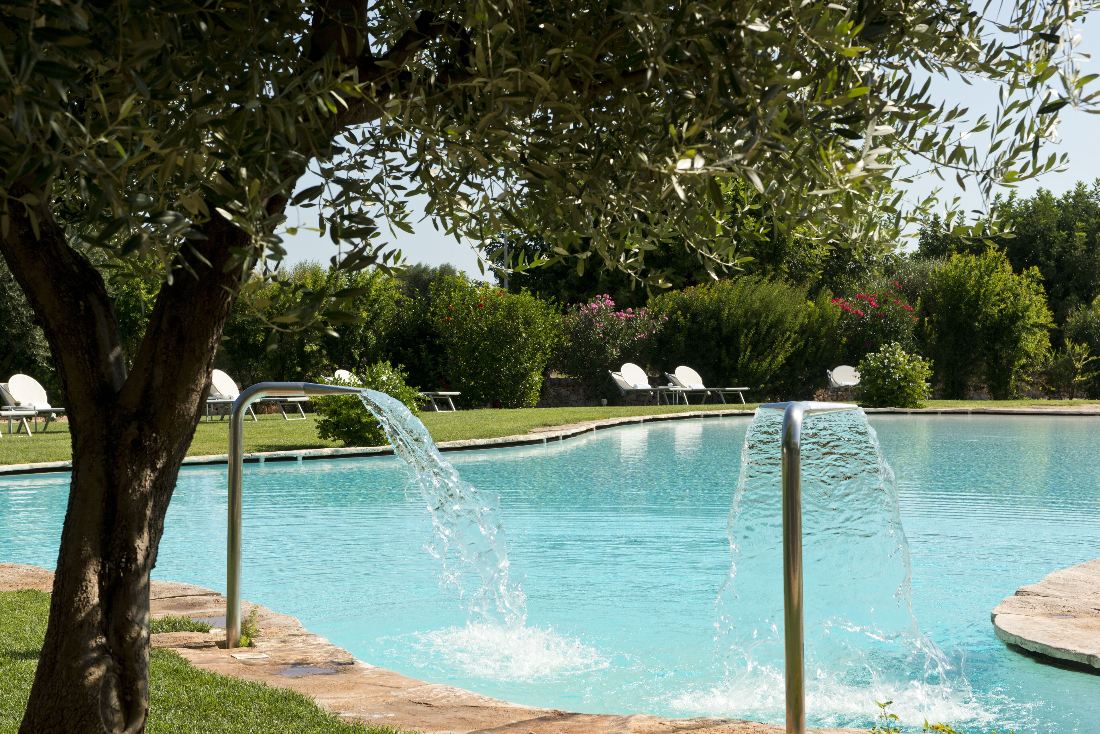 A swimming pool with a water feature, surrounded by greenery and lounge chairs.