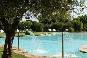 A swimming pool with a water feature, surrounded by greenery and lounge chairs. - Masseria Don Luigi - Luxury Farmhouse (Fasano)