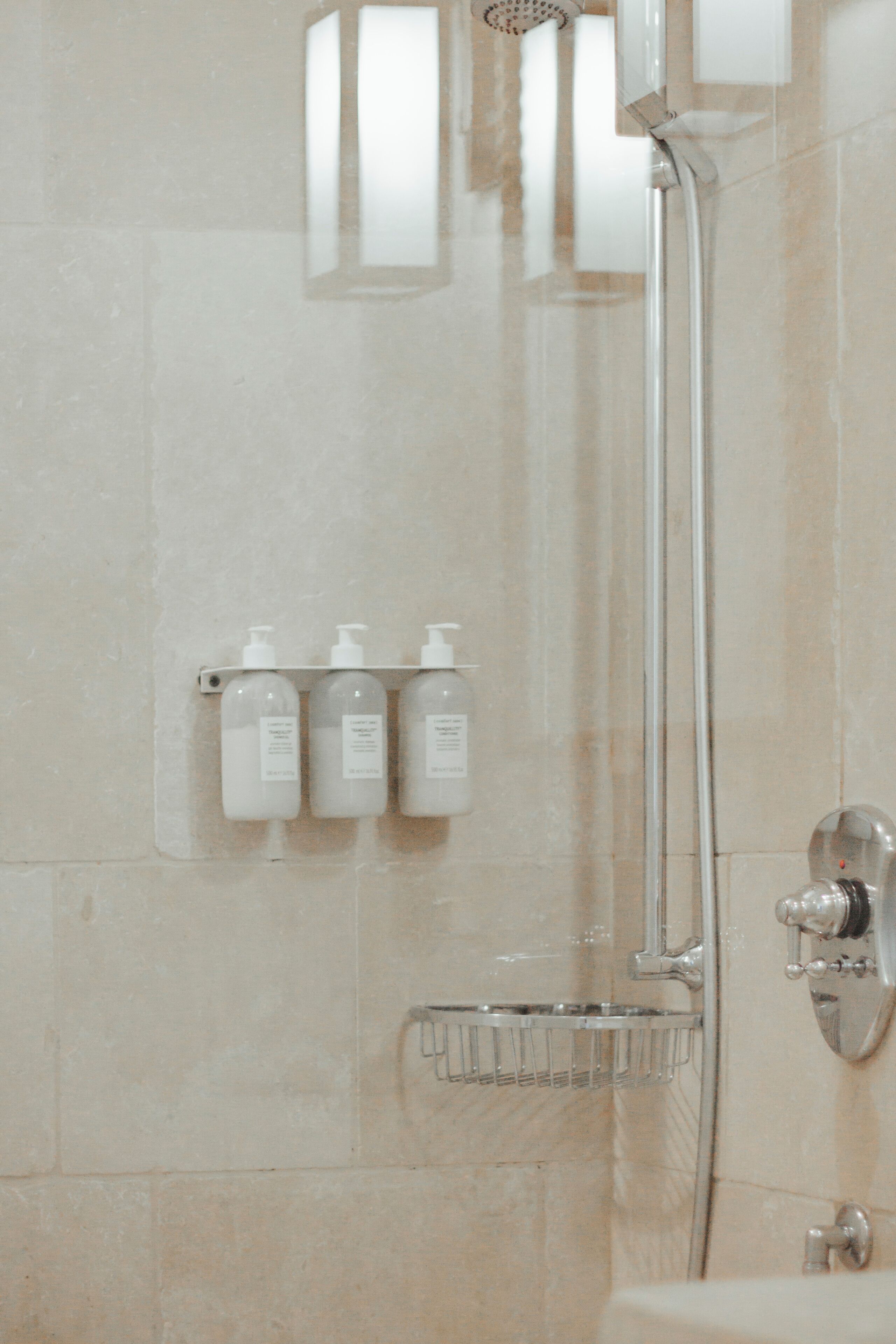 Ein Badezimmer mit Dusche, Waschbecken und drei Shampooflaschen an einem Wandregal.