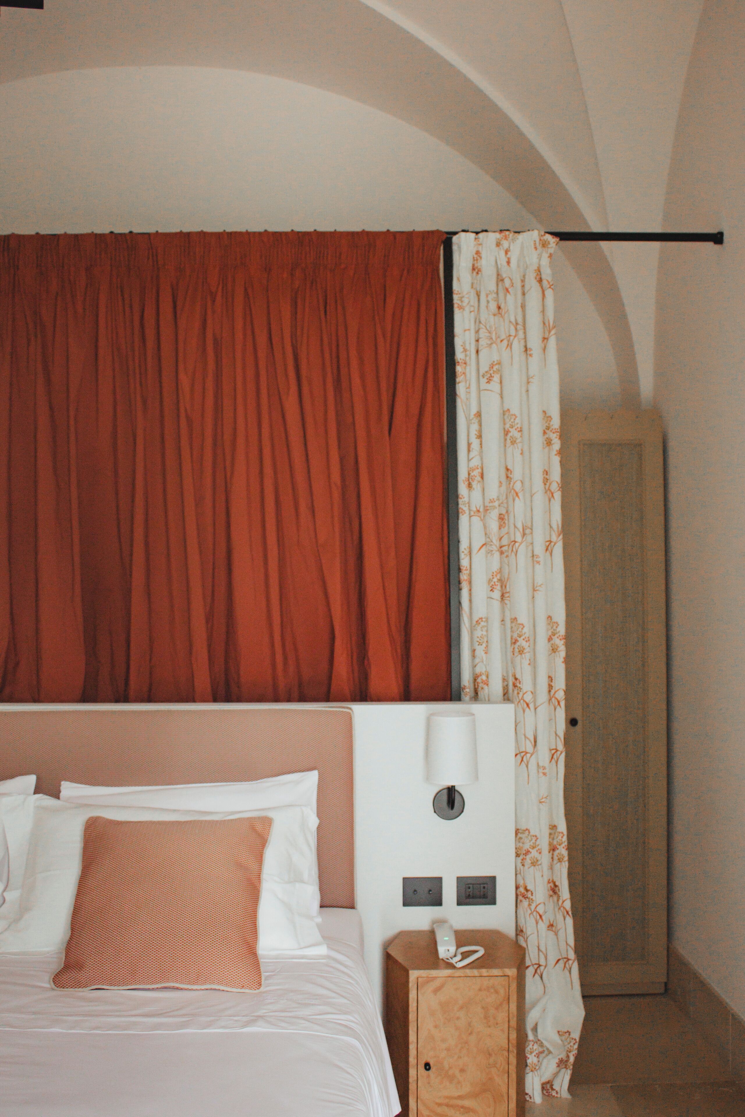 A hotel room with a bed, a nightstand, a telephone, and a wardrobe.