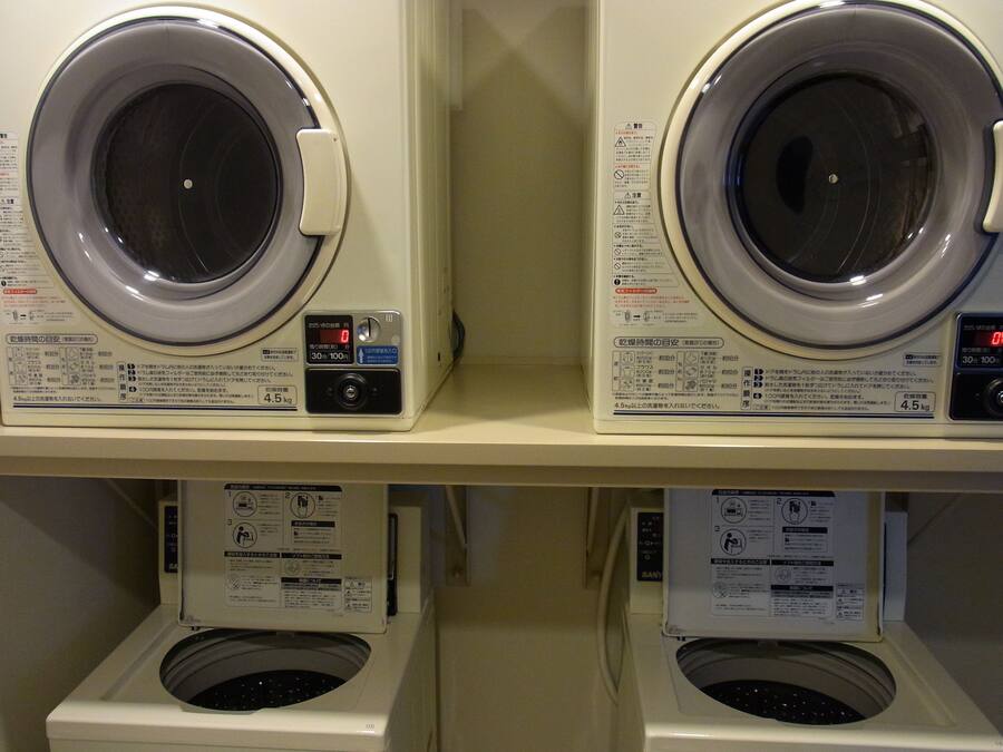 Two front-loading washing machines on a shelf, each with a control panel and instruction manual.
