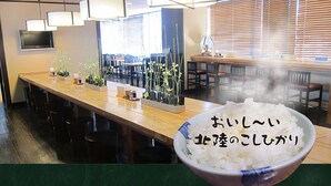 Interior de restaurante com balcão comprido, cadeiras e uma tigela de arroz com texto em japonês.